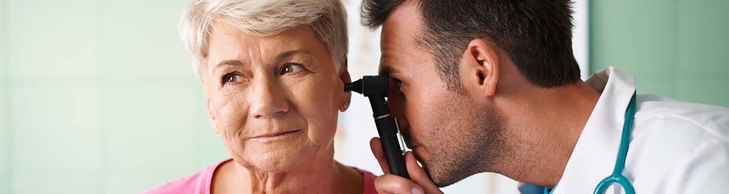 senior woman with white hair looking to the left, male doctor looking in her ear with a otoscope