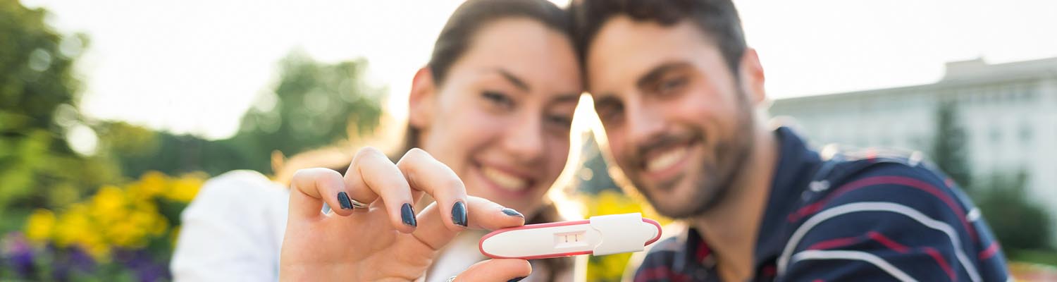 Young couple smiling and holding up a positive pregnancy test