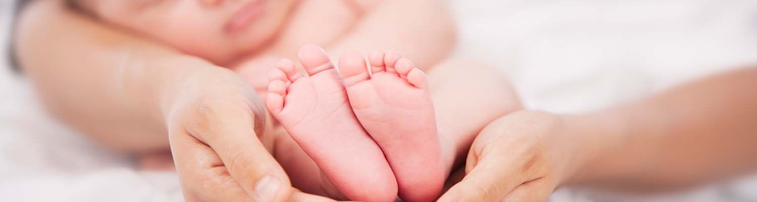 Close up of bare baby's feet cradled by mom's hands