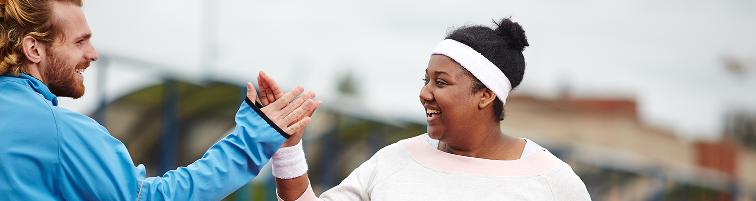  Happy plus-size woman giving high five to her personal trainer while running on track 