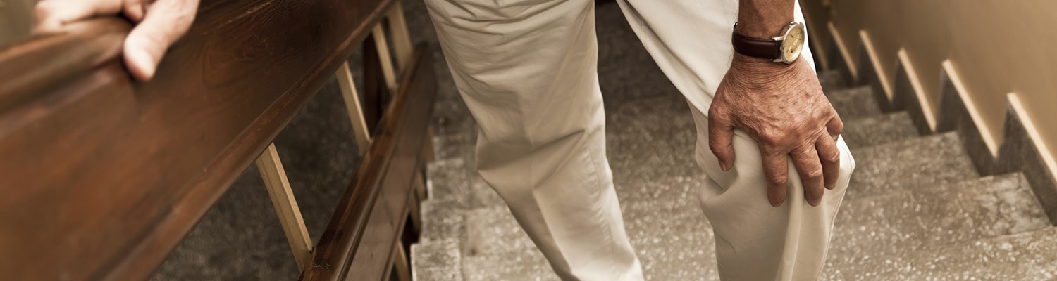 Closeup of man's legs in beige pants walking upstairs. Hand held on one knee.
